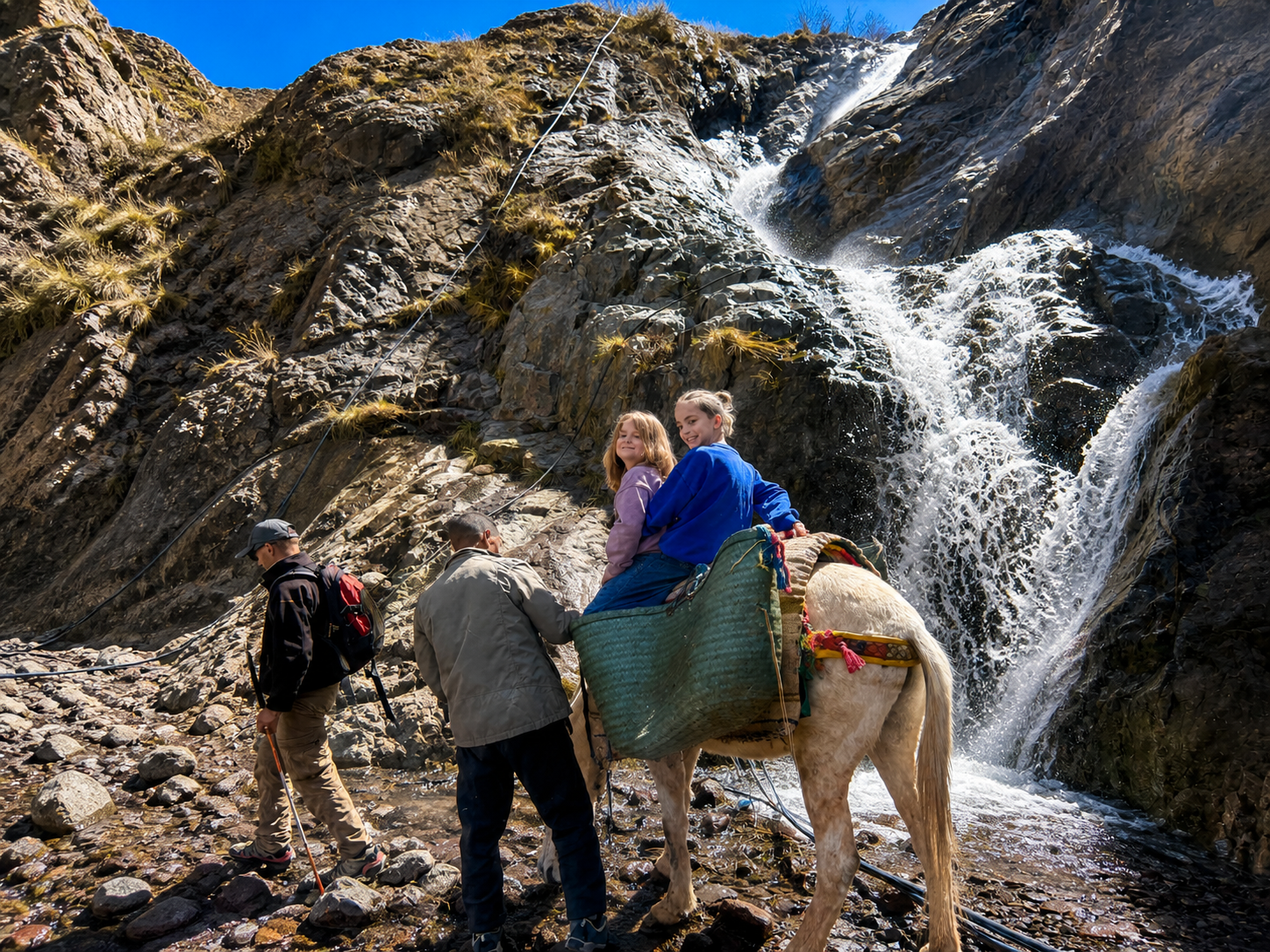 Kinderen op ezeltocht langs een waterval in het Atlasgebergte van Marokko