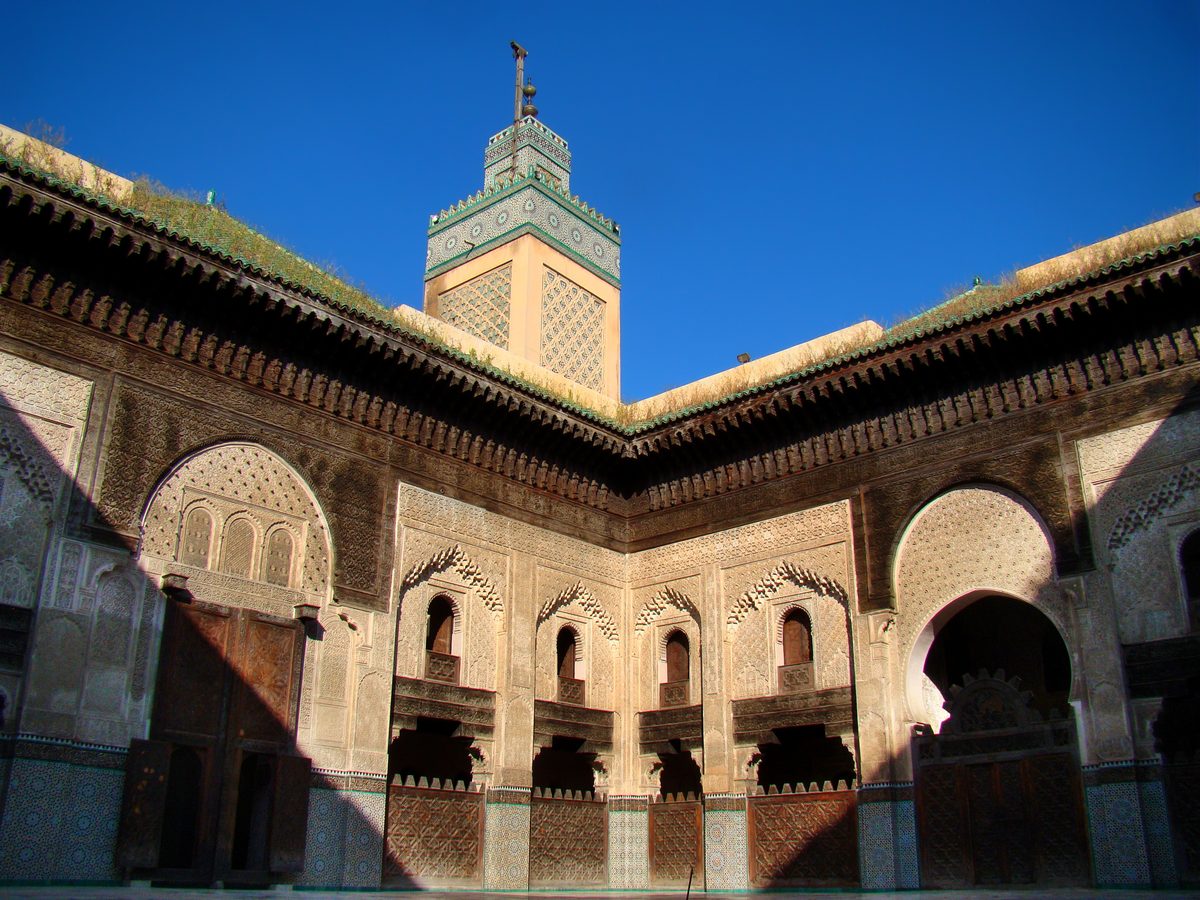 Binnenplaats Bou Inania Madrasa Fès Marokko met sierlijk gesneden stucwerk houten galerijen groene daktegels en minaret