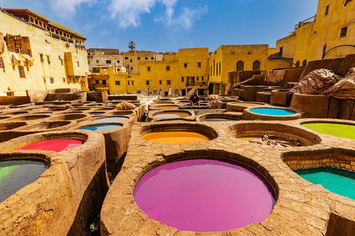 Leerlooierijen Fès Marokko van opzij met roze oranje blauwe turquoise kuipen arbeiders en gele gebouwen rondom