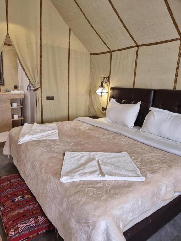 Slaapkamer luxe woestijntent Merzouga Zagora Erg Chebbi Cheggaga Merzouga Marokko met groot bed witte lakens Marokkaanse wandlamp en Berbertapijt