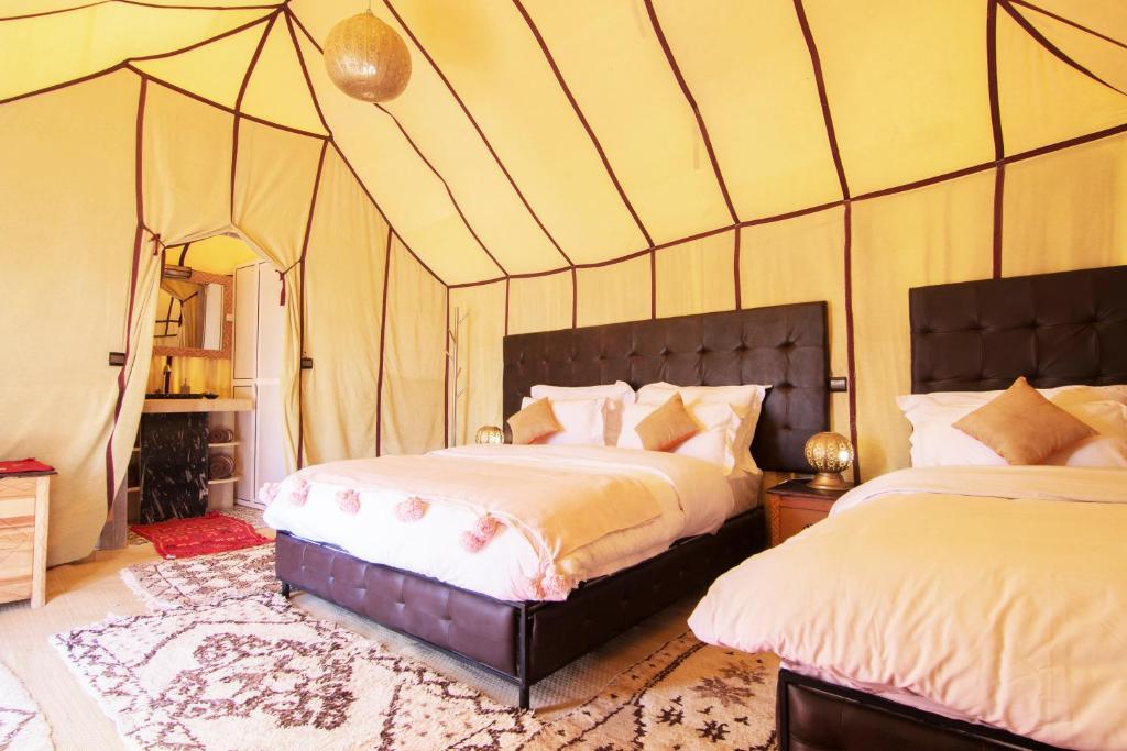 Interieur luxe woestijntent Merzouga Zagora Erg Chebbi Cheggaga Marokko met twee bedden gouden hanglamp roze kussens en traditioneel Berbertapijt