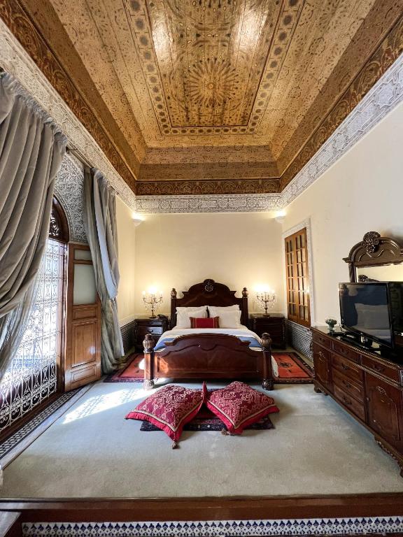 Traditionele riad slaapkamer Fès Marokko met rijk gesneden houten plafond vierpostbed rode kussens en Marokkaans interieur
