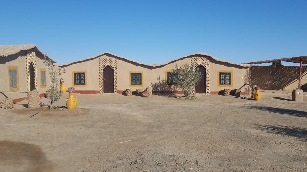 Eenvoudig woestijnverblijf Merzouga Zagora Erg Chebbi Cheggaga Marokko exterieur leemgebouw boogdeuren gele aardewerken potten en heldere blauwe lucht