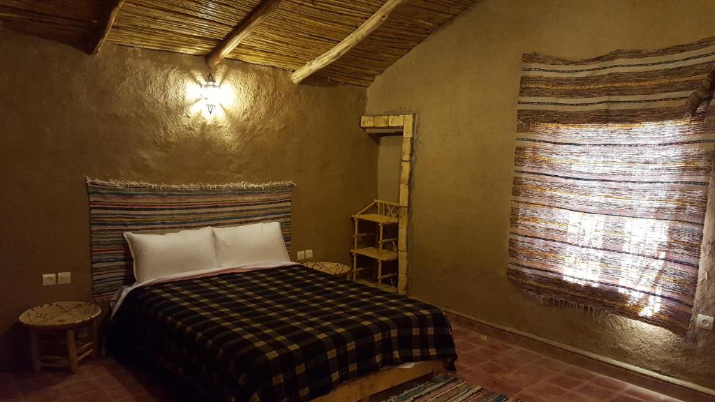 Authentieke woestijnslaapkamer Merzouga Zagora Erg Chebbi Cheggaga Marokko met tweepersoonsbed geblokt deken leemwanden rietplafond en Berberkleed als hoofdbord