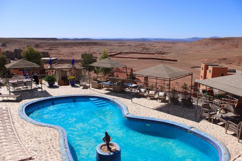 Kasbah hotel zwembad Marokko met uitzicht op rotsachtig woestijnlandschap ligstoelen pergolas en heldere blauwe lucht