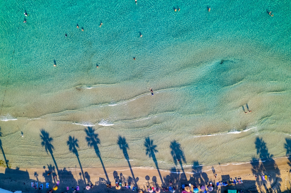 Luchtfoto van een strand bij Kuşadası met palmschaduwen op het zand en zwemmers in turquoise water