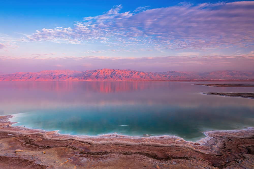 Dode Zee met spiegelend water en bergketen in roze licht aan de overkant
