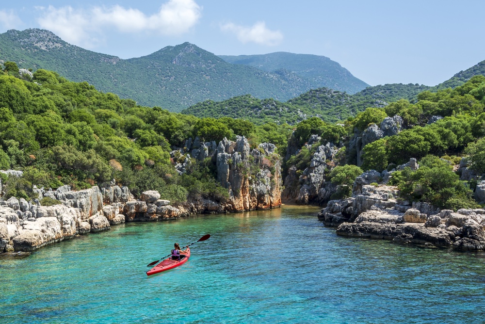 Kajakker in een rode zeekajak op turkoois water in een beschutte baai bij Kaş