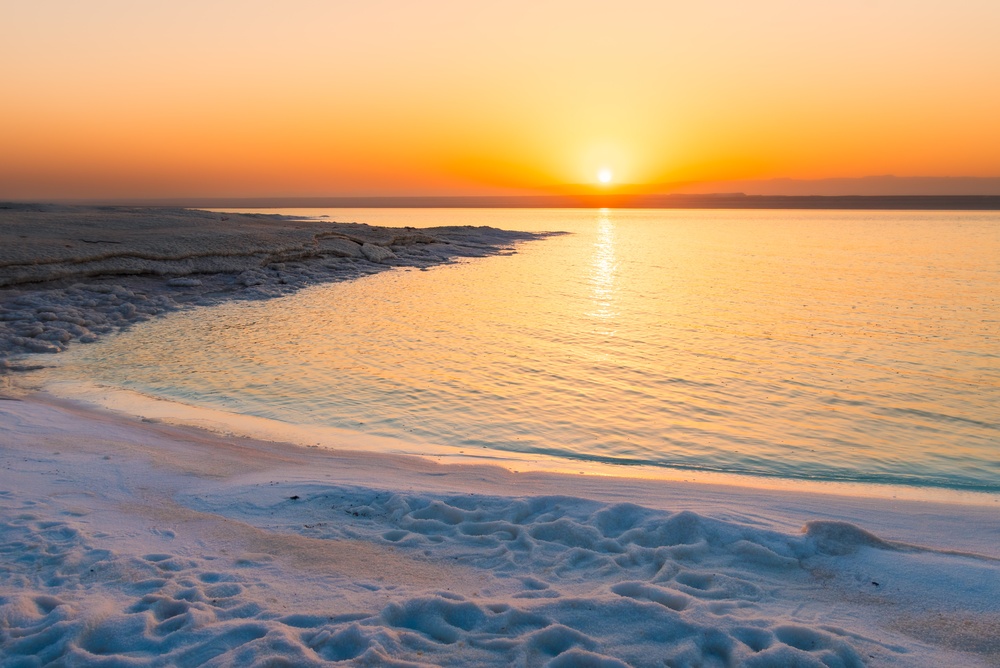 Zoutkorst langs de oever van de Dode Zee met laagstaande zon boven het water