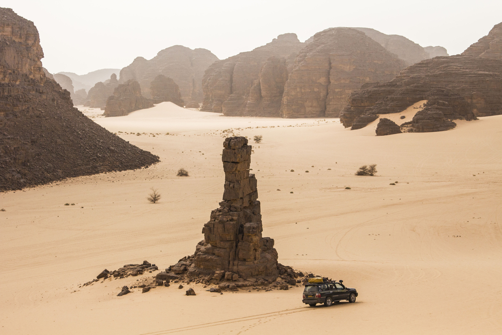 Terreinwagen naast een alleenstaande rotspilaar in de woestijn bij Tamanrasset