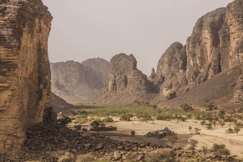 Zandsteenmassieven rond een vallei met acacia's en stenen onderkomens bij Djanet in de Tassili n'Ajjer